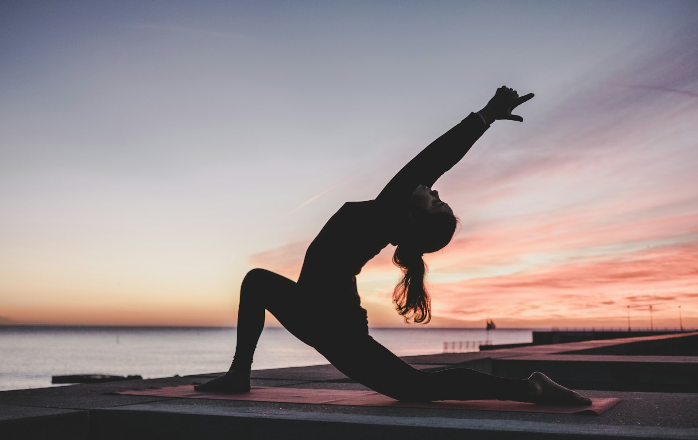 Silueta de una mujer practicando yoga frente al mar al atardecer
